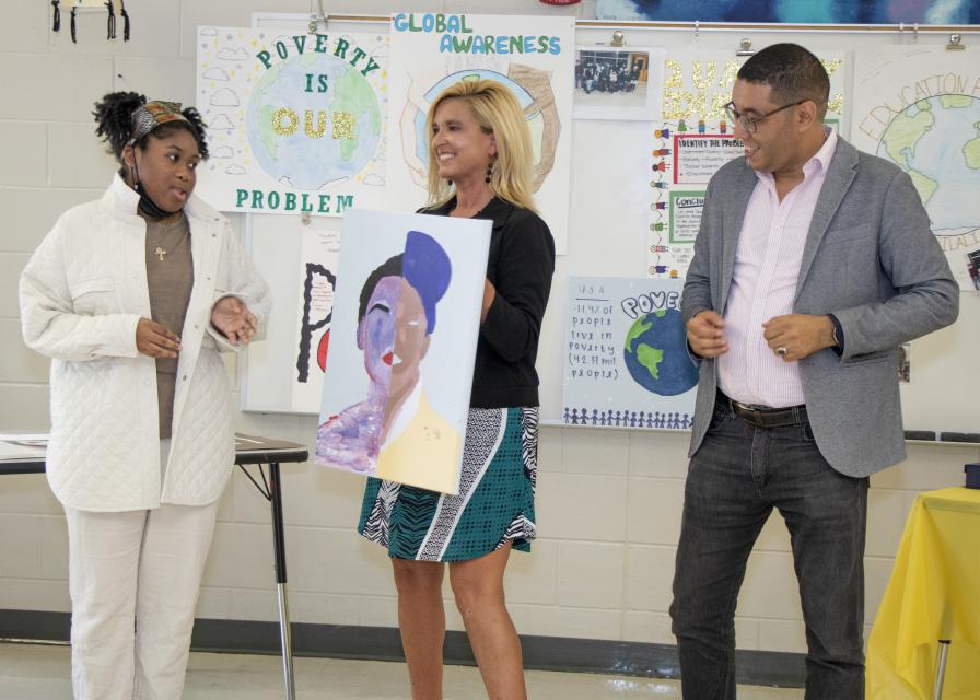 A student presents a painting while Dr. Peele and another educator look on.