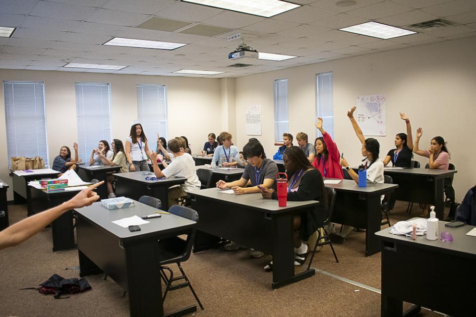 Students in classroom raising their hands.