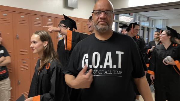 Johnson stands among Orange High School graduates pointing to his shirt, which reads “G.O.A.T. - Greatest of All Time.”