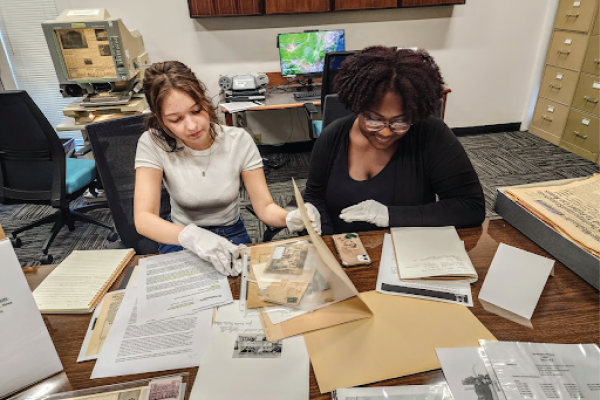 Two high school students wear gloves while examining historical documents.