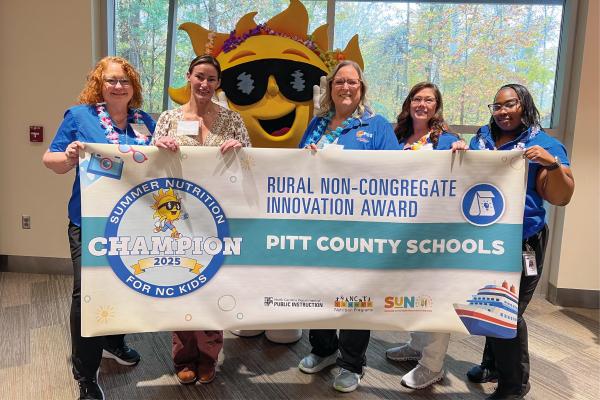 Members of the Pitt County Schools nutrition staff hold a banner that recognizes their district for receiving a Rural Non-Congregate Award.