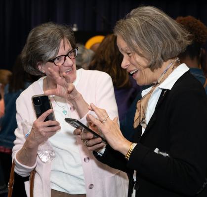 Two women conversing while holding cell phones.