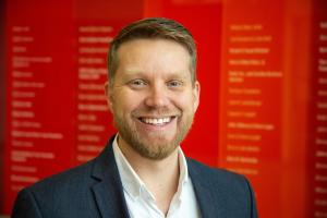 A headshot of Shaun Kellogg in front of a red background.