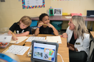 Teacher, Hannah Moon, kneeling by a desk working with students