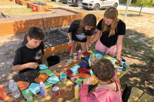 Four students paint on an outside picnic table.