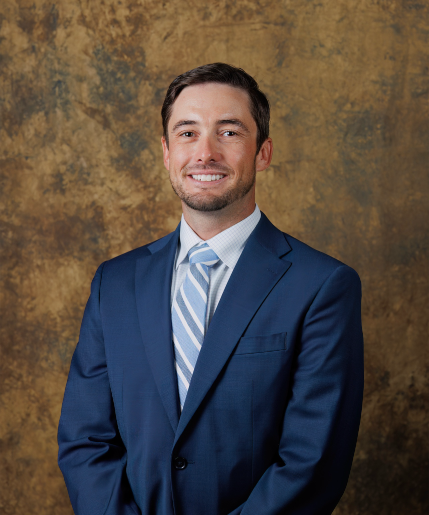 justin boyd poses in a blue suit and tie in front of a mottled bronze background