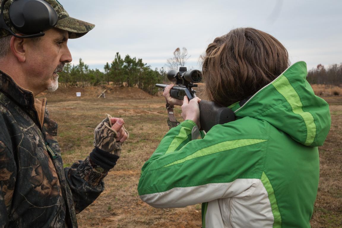 A NCWRC staff member assists a student learning to aim their rifle.
