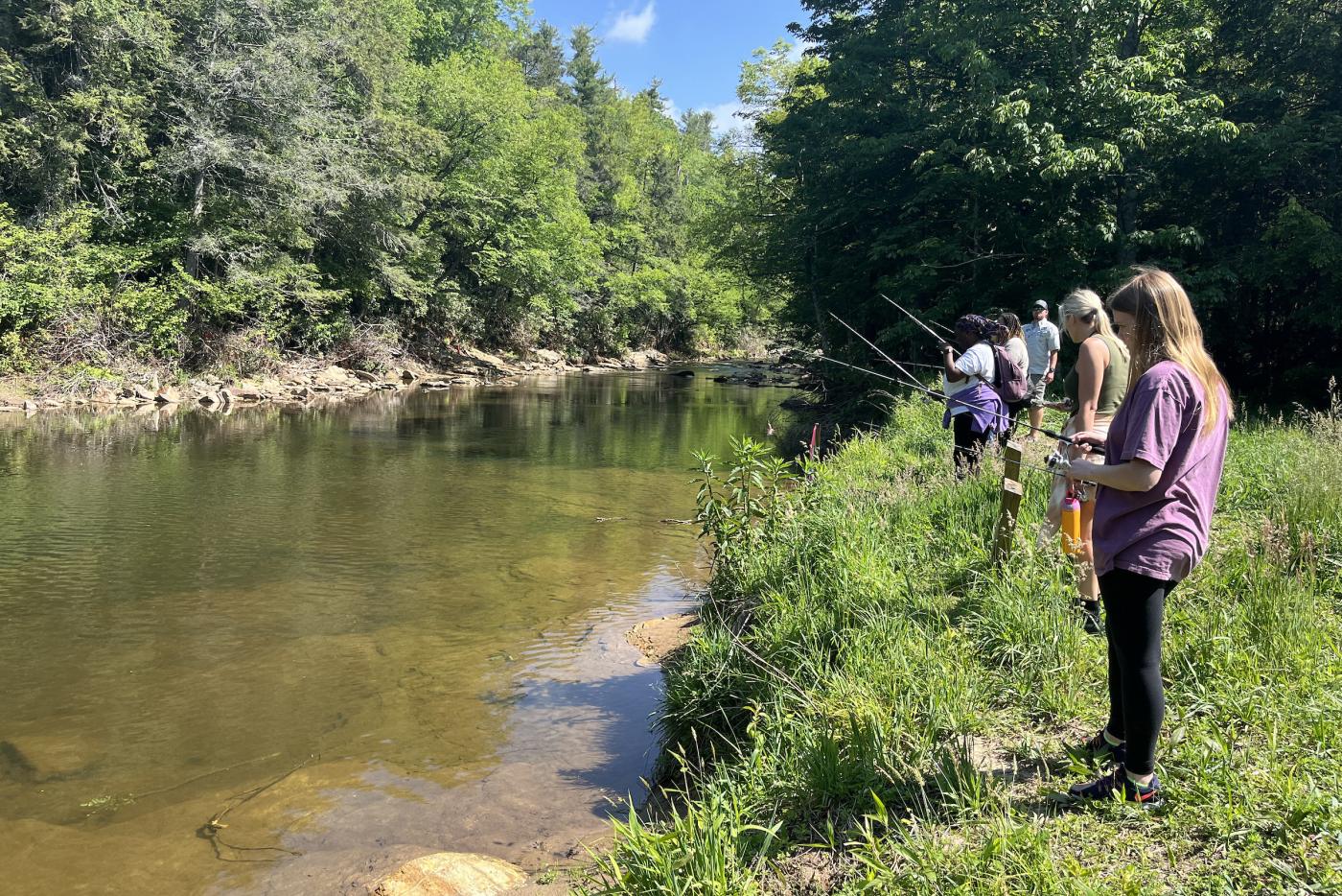 Several people stand at the shore fishing in shallow water