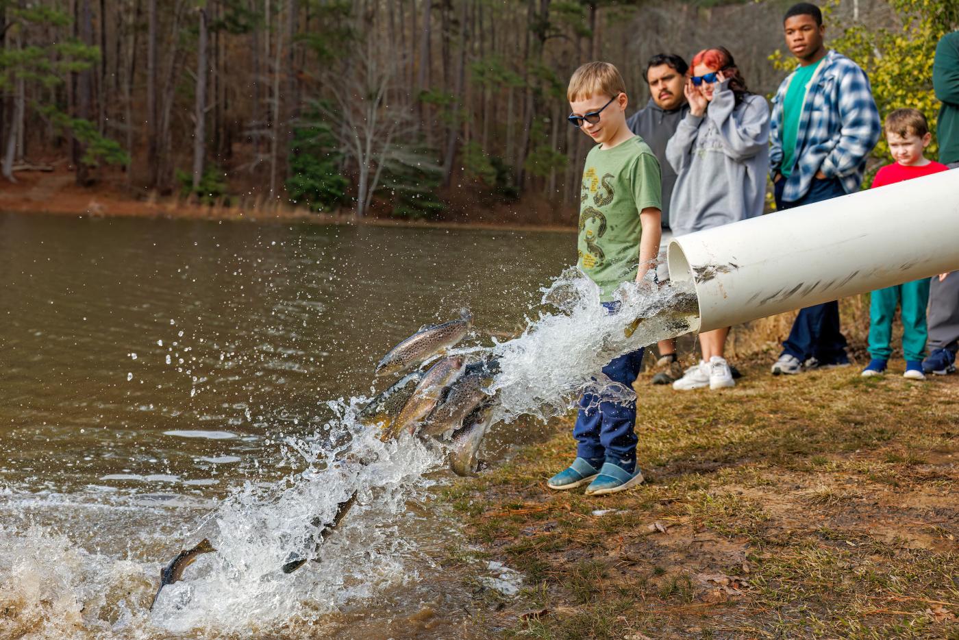 onlookers observe trout being released into a pond through a large tube