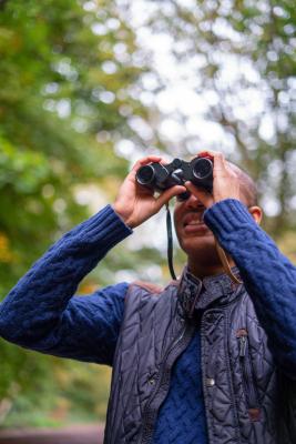 A man holds a pair of binoculars over his eyes while looking for birds in a wooded area
