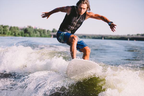 A man wake surfs on a lake behind a boat.