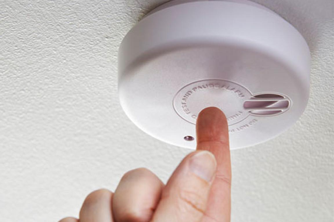 Hand and finger about to test a smoke detector
