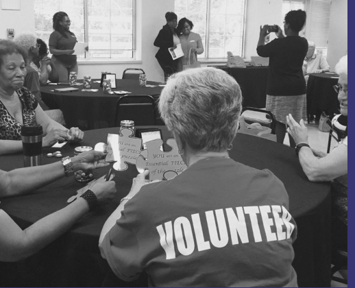 Group of volunteers in a meeting room, one wearing a VOLUNTEER shirt
