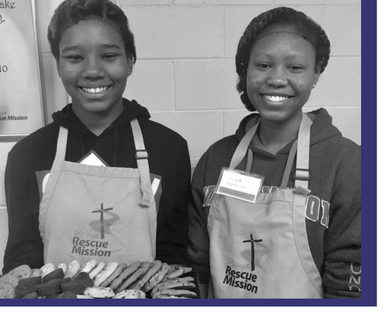 Two young volunteers posing for a photo wearing aprons