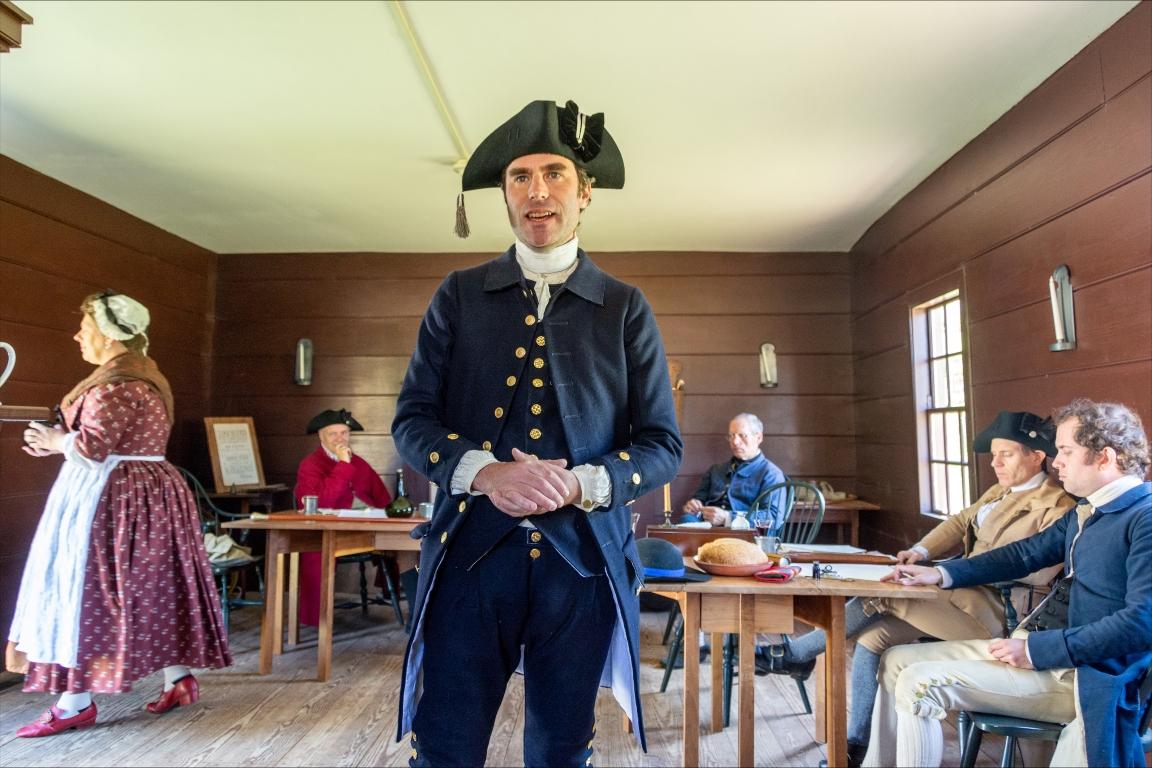 Halifax Resolves reenactment with men and women wearing colonial clothing in a room