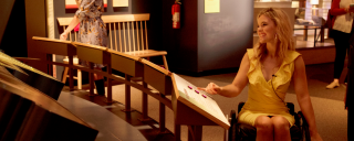 A woman in a wheelchair looking at an exhibit panel in a museum. 