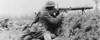 Two World War I machine gunners fire over a trench wall