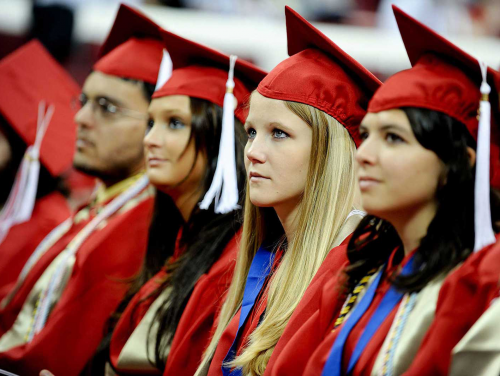 a young man and 3 young women in red graduation caps and gowns