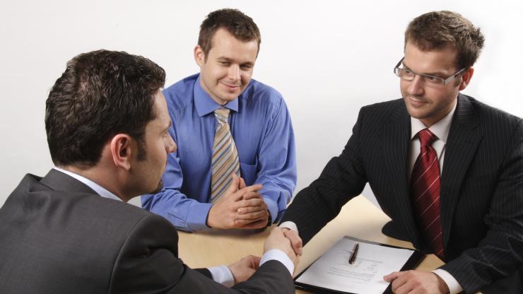 young men sitting at table shaking hands