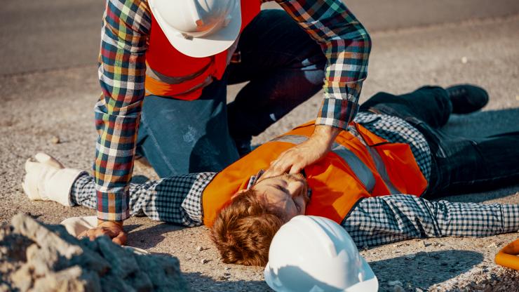 worker in hard hat checks vital signs of injured co-worker