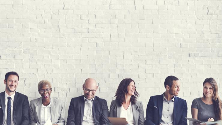 men and women in business attire in front of a white brick wall