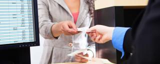 Two people exchanging deposit slip One person handing another person a receipt at a bank window