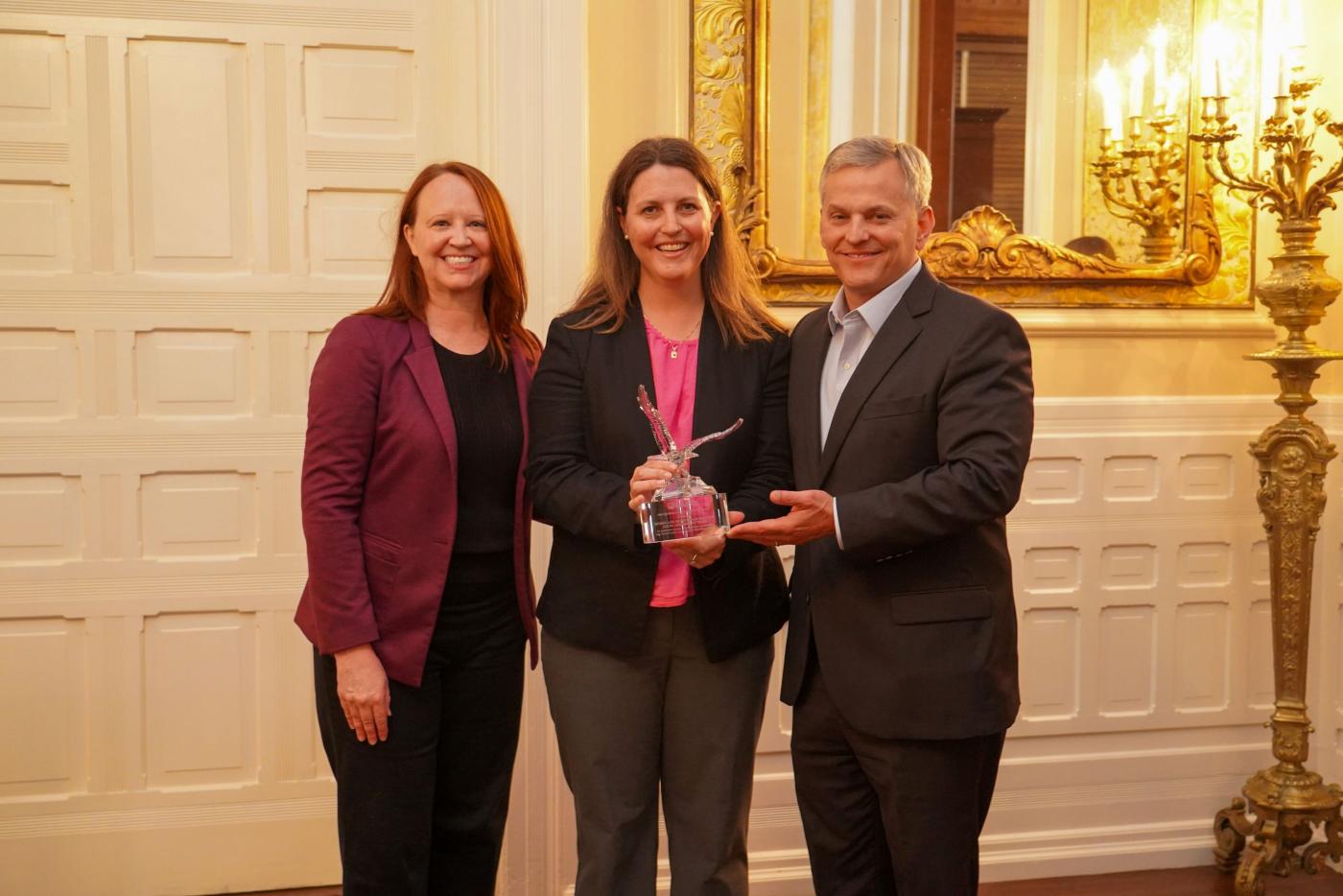 A man and two women smiling and standing close together holding a crystal trophy shaped like an eagle