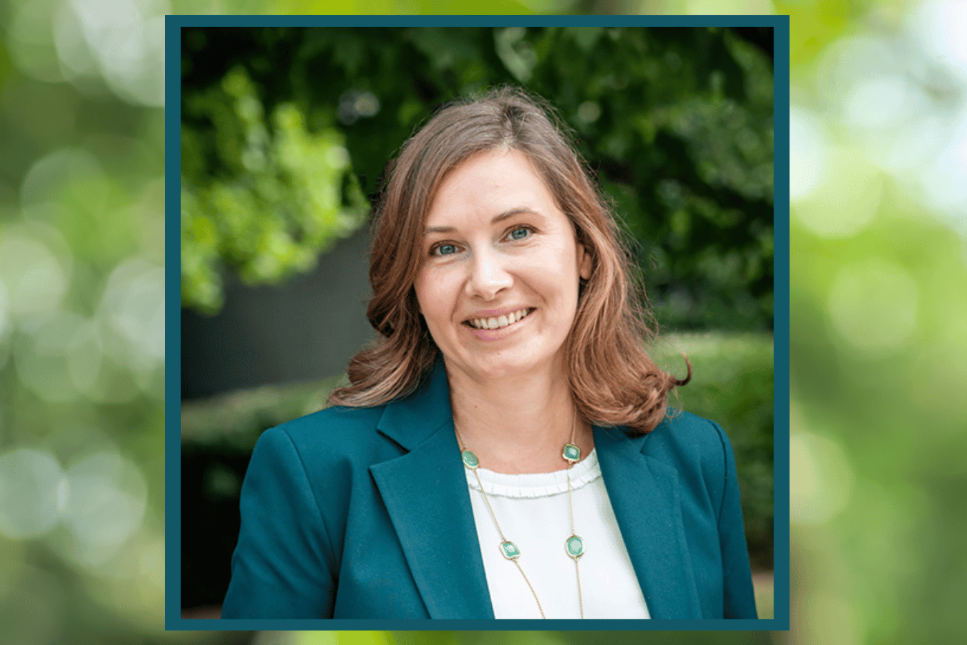 Headshot of woman smiling in front of dark green foliage