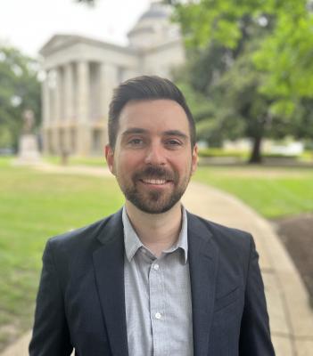 Nathan Heim, man, facing forward, smiling, building and trees in background