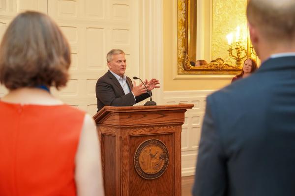 Man speaks at a podium, as people look on