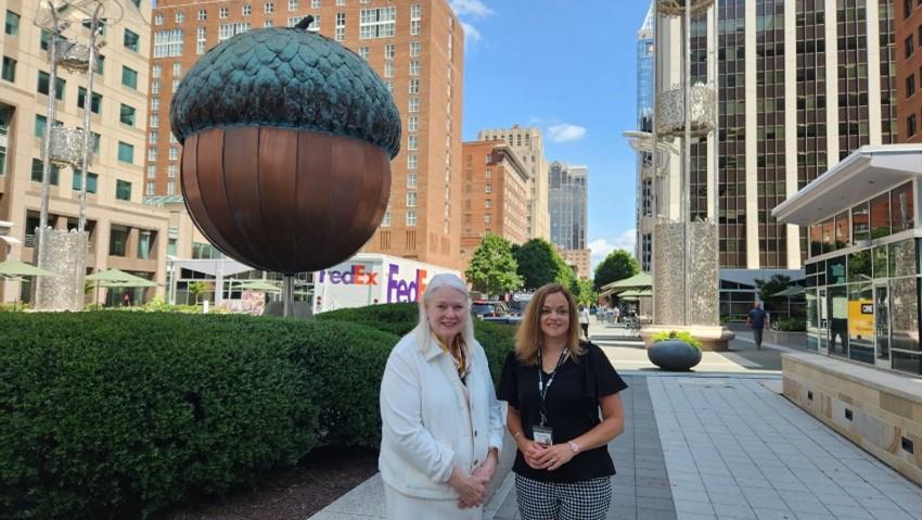 State Human Resources Director Staci Meyer and journalist Dawn Baumgartner Vaughan pose in front of a giant acorn in downtown Raleigh.