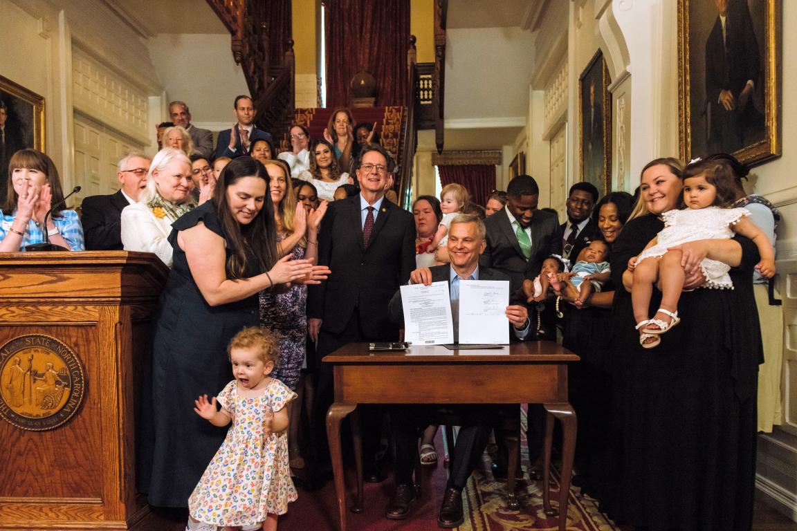 Governor Josh Stein displays signed S1041 as the crowd applauds.