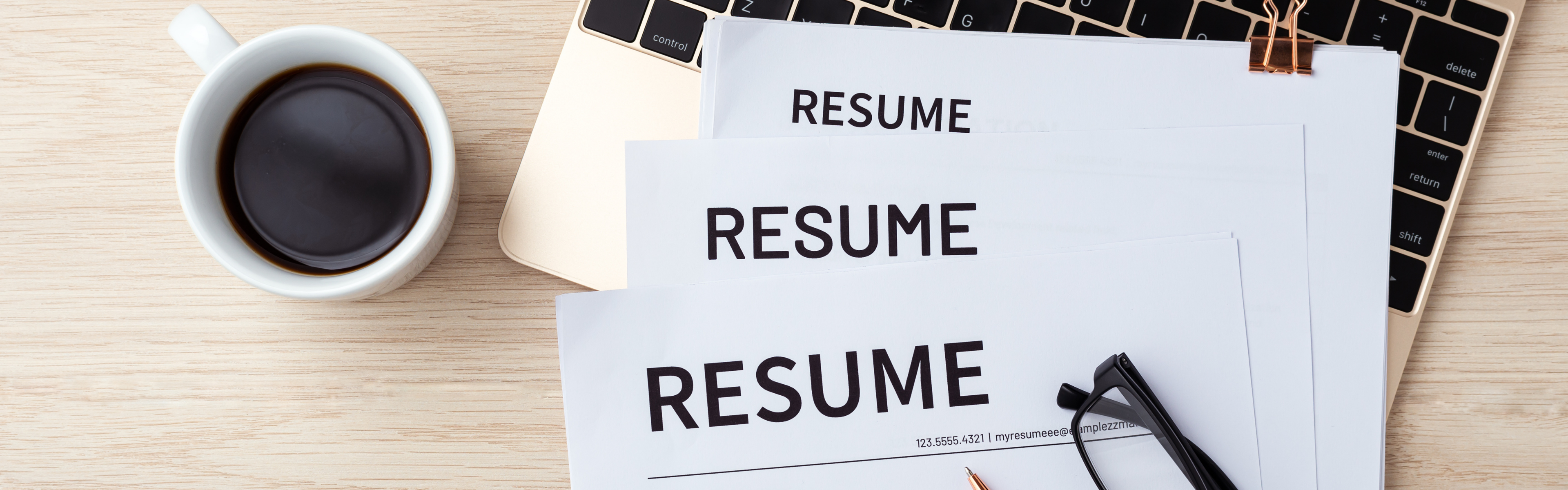 Resume on desk with laptop and coffee.