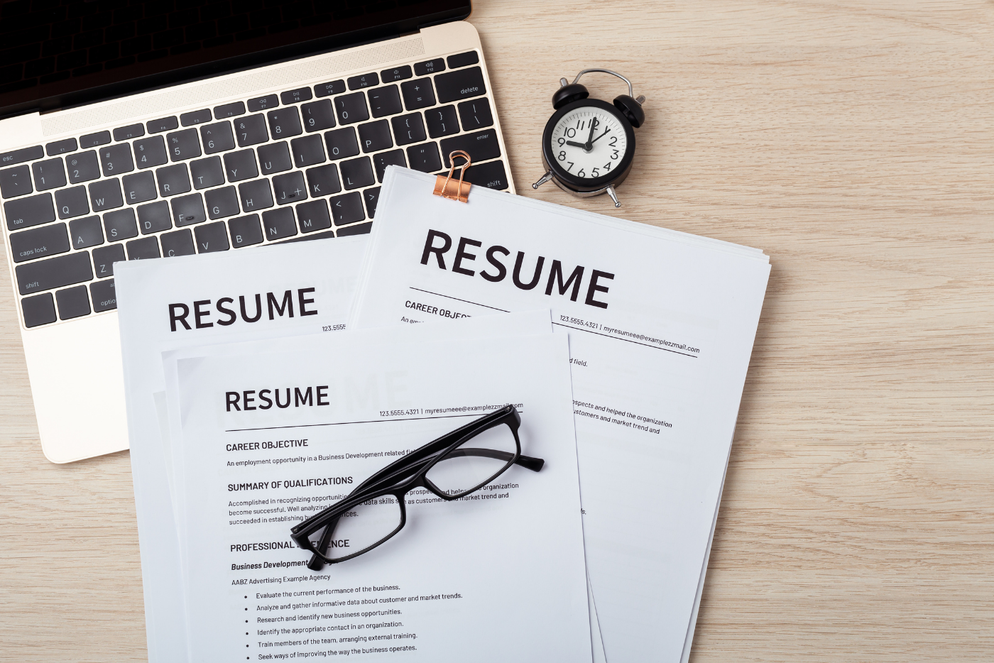 Resume on desk with pens and laptop and glasses.