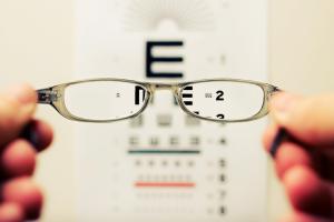 Hands holding glasses in front of an eye chart.