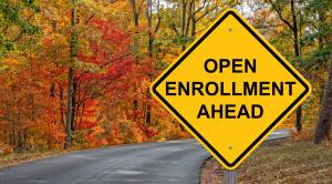 Image of a road, lined with fall colored trees. At the front of the image is a yellow road sign that says "Open Enrollment Ahead"