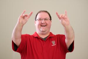 Man in red shirt making NC State wolfpack sign with his hands.