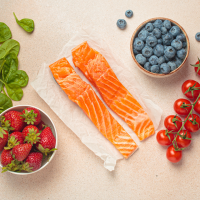 spinach leaves, bowl of strawberries, two pieces of uncooked salmon, bowl of blue berries, and some small tomatoes