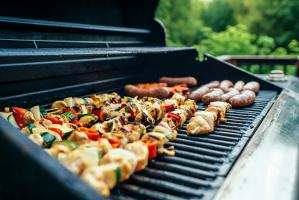 side view of a grill which has kabobs laying on it and hotdogs