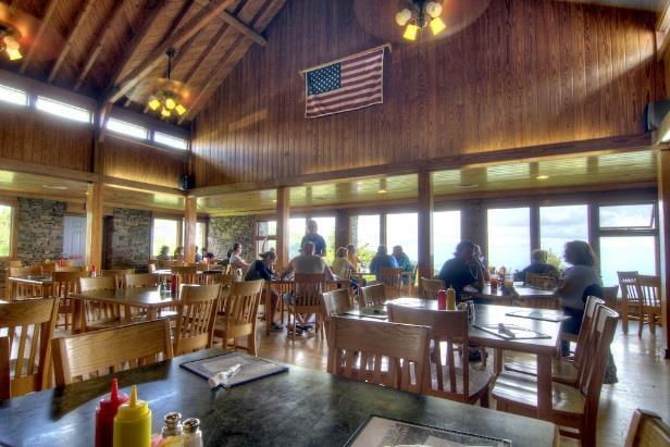 Interior view of the restaurant dining area featuring wooden chairs, tables, large scenic windows, and an American flag hanging from the log rafters