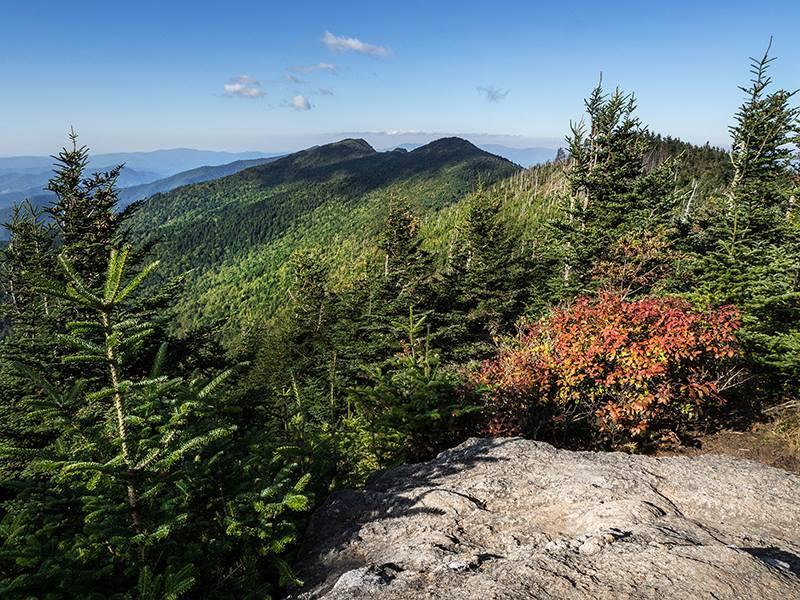Summit of Mount Mitchell showing rock outcroppings and evergreen trees in the foreground with layered mountain ridges fading into the distance