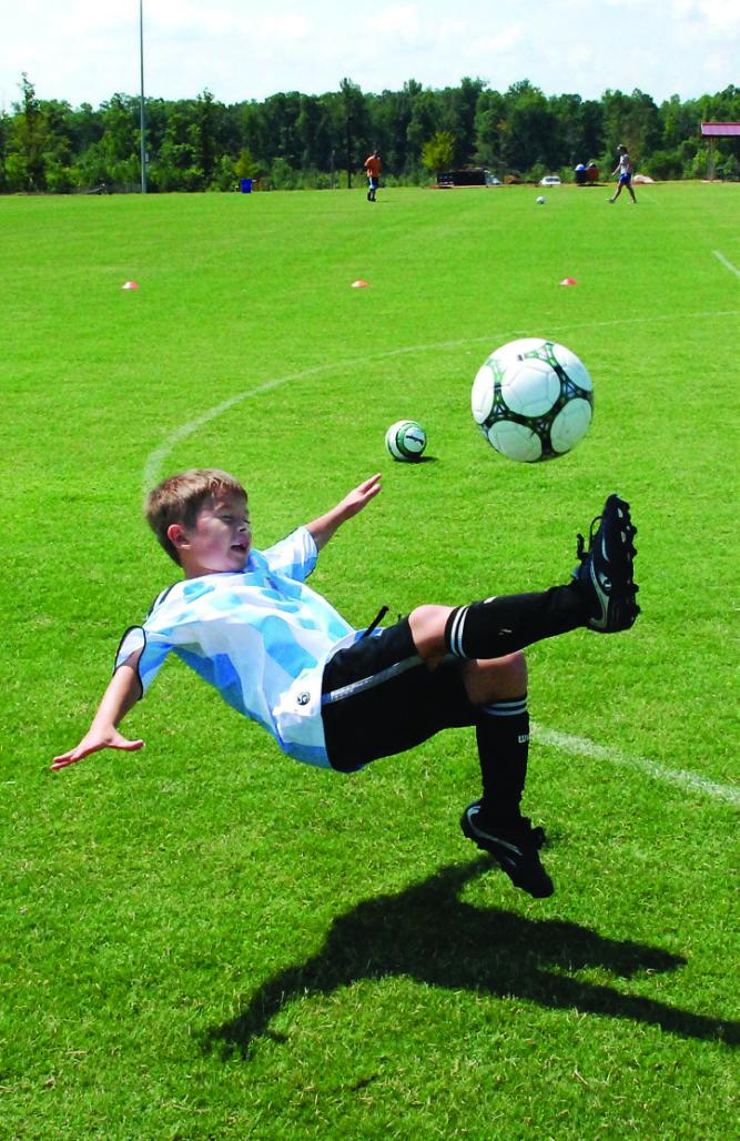 Photo of a young boy falling backwards while kicking a soccer ball