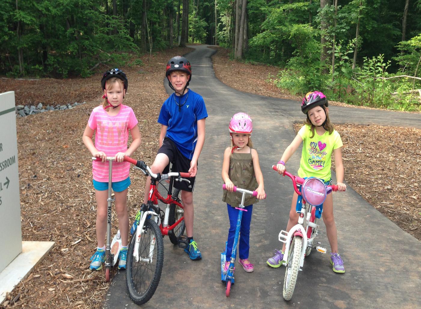 Photo of four children posing with scooters and bikes on a path at Rock Springs Nature Preserve