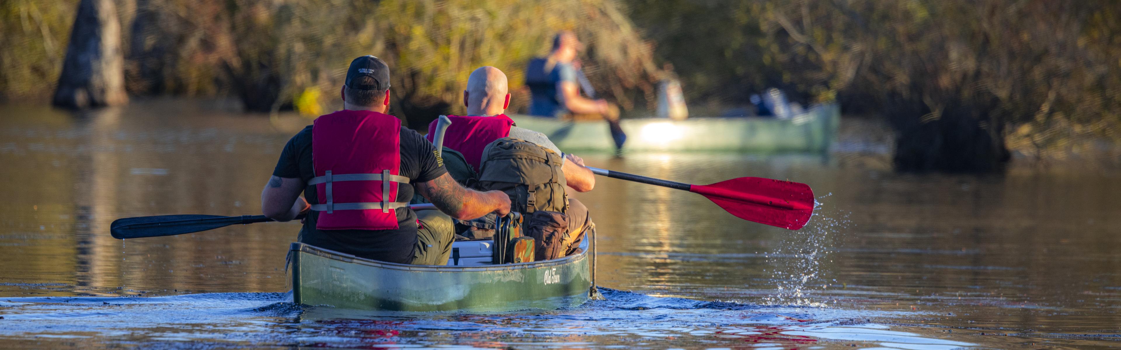 Kayakers in red life jackets head out on the millpond with camping gear