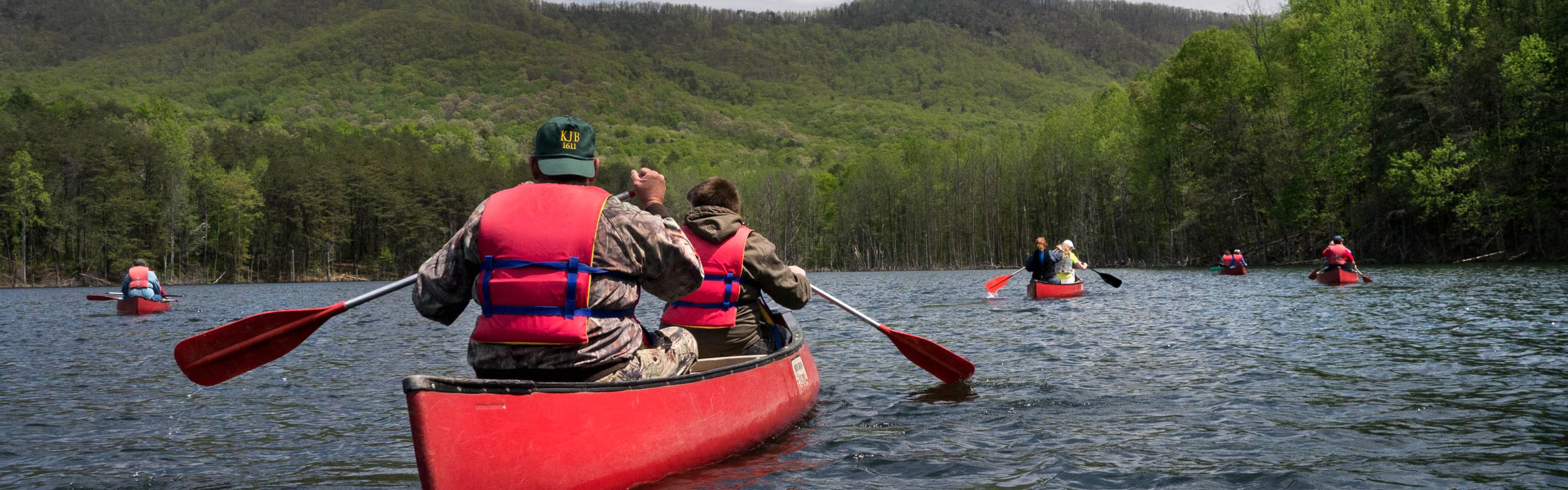 People in a red canoe paddle on a lake with mountains in the background on a partly cloudy day