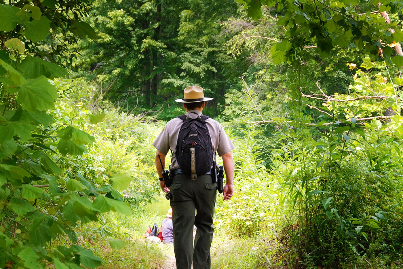 Ranger with a backpack hiking on a trail at Eno River State Park