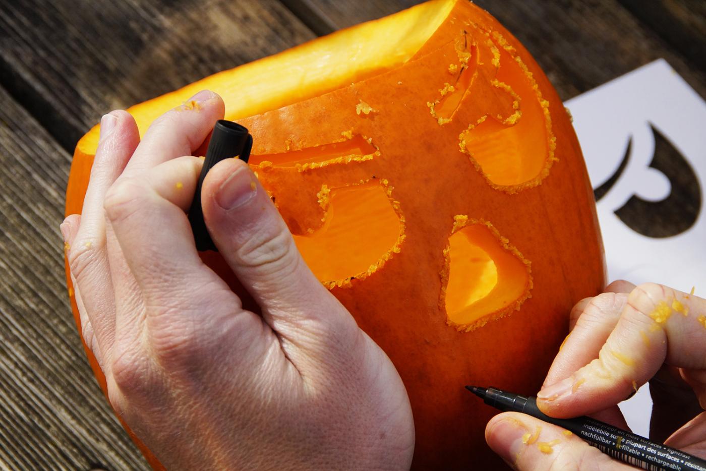 Person's hand holding and drawing on a pumpkin to carve a face