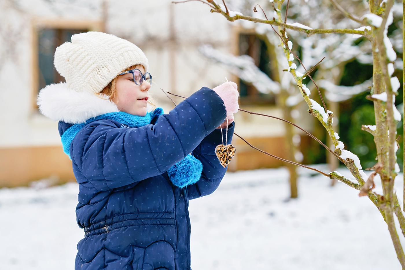 Girl hanging a bird seed bar on a snowy tree in the winter.