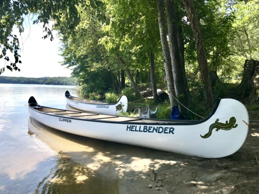 Two large canoes, named Hellbender and Loggerhead, are docked along the lake shoreline.