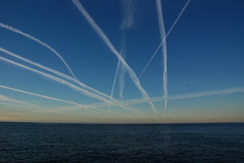 Ocean surface with blue sky and multiple white airplane contrails above